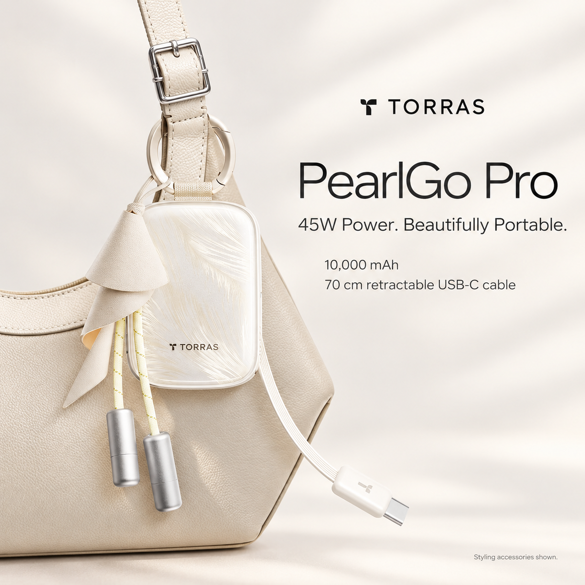 PearlGo Pro Pearl White power bank clipped to a cream handbag, with feather finish and retractable USB-C cable; styling accessories shown